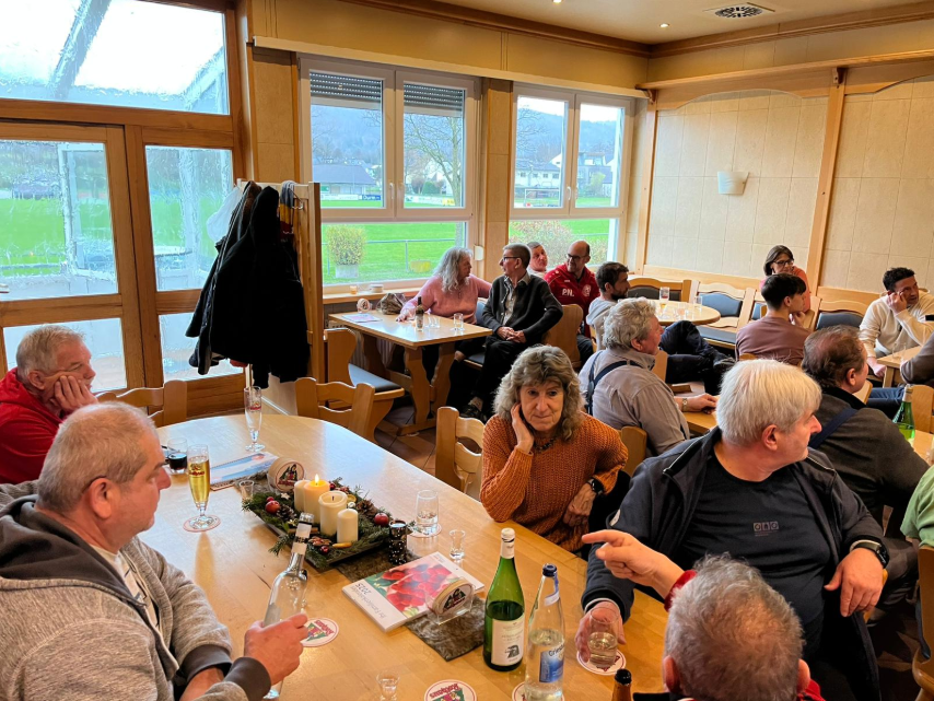 Eine Gruppe von Personen sitzt an einem Restauranttisch und genießt ihr Essen und die Gesellschaft der anderen in einer warmen Umgebung.