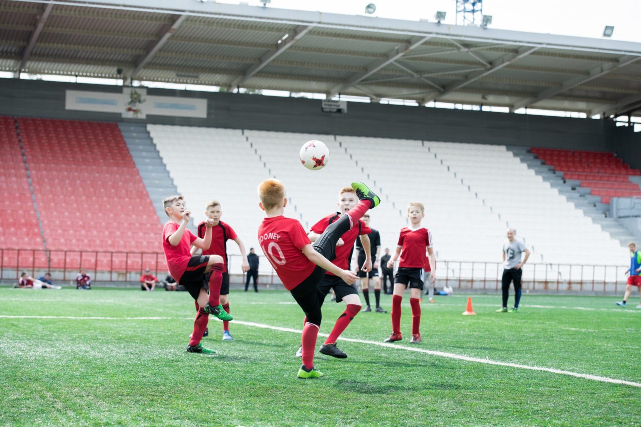 Eine Gruppe von Jungen spielt auf einer Wiese unter strahlend blauem Himmel energisch Fußball.