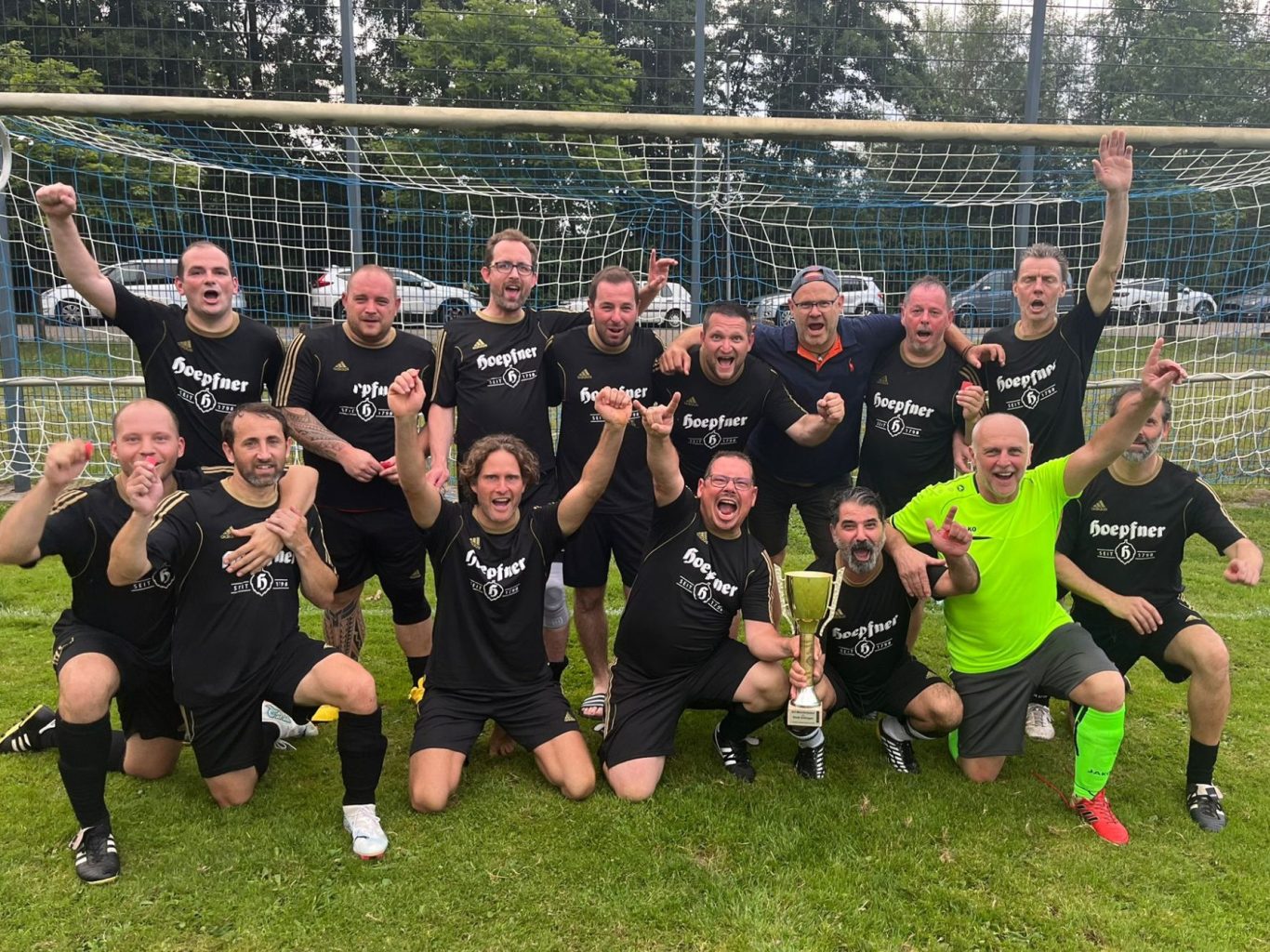 Eine Gruppe von lächelnden Männern, die gemeinsam vor einem Fußballtor posieren und Kameradschaft und Teamgeist demonstrieren.