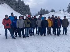 Eine Ansammlung von Personen in Winterkleidung, die in einer verschneiten Gegend stehen, umgeben von einer ruhigen Winterumgebung.