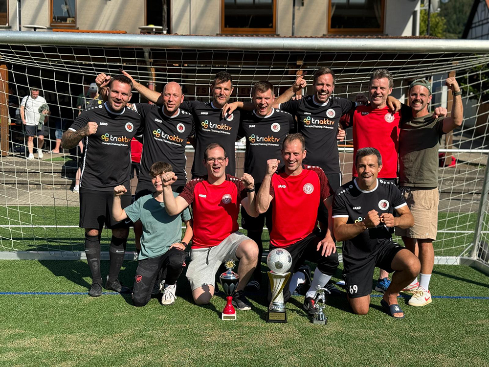 Männergruppe steht vor einem Fußballtor und lächelt für ein Gruppenfoto.