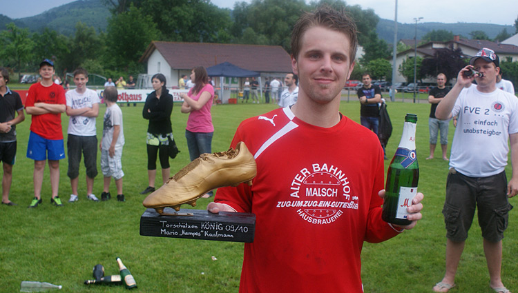 Ein Mann hält einen Pokal in der einen Hand und eine Flasche Champagner in der anderen Hand, strahlend vor Freude