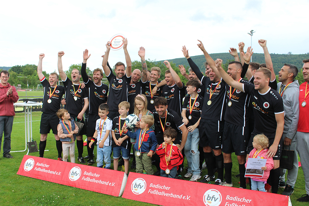 Eine Gruppe von Menschen steht auf einem Feld und hält stolz einen Pokal in den Händen.