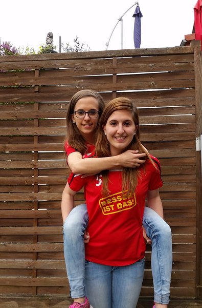 Zwei junge Frauen in roten T-Shirts stehen zusammen und lächeln für ein Bild.
