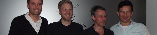 Vier Männer stehen aufrecht vor einer weißen Wand und zeigen verschiedene Posen.