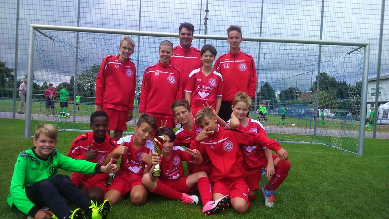 Eine Gruppe junger Fußballspieler posiert lächelnd für ein Foto auf dem Spielfeld.