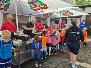 Man sieht die Helfer in einer Reihe bei der Essensausgabe und eine Schlange von Kindern, die sich für das Essen in einer Reihe anstellen